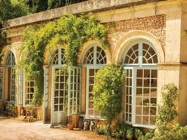 A stone orangery with arched windows and climbing greenery in warm afternoon light