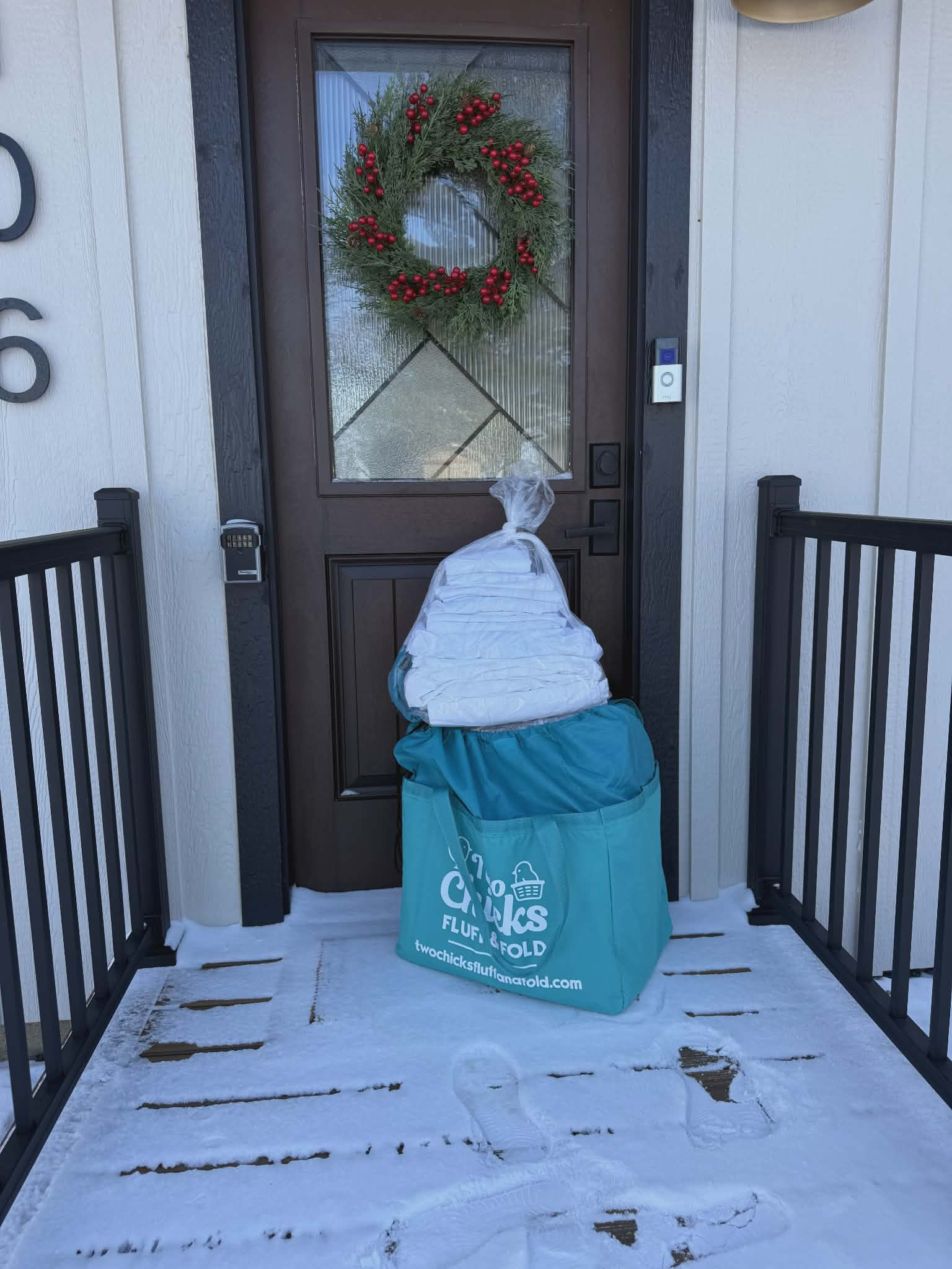 A teal Two Chicks Fluff and Fold laundry bag with finished laundry delivered to a customer's snow-covered porch