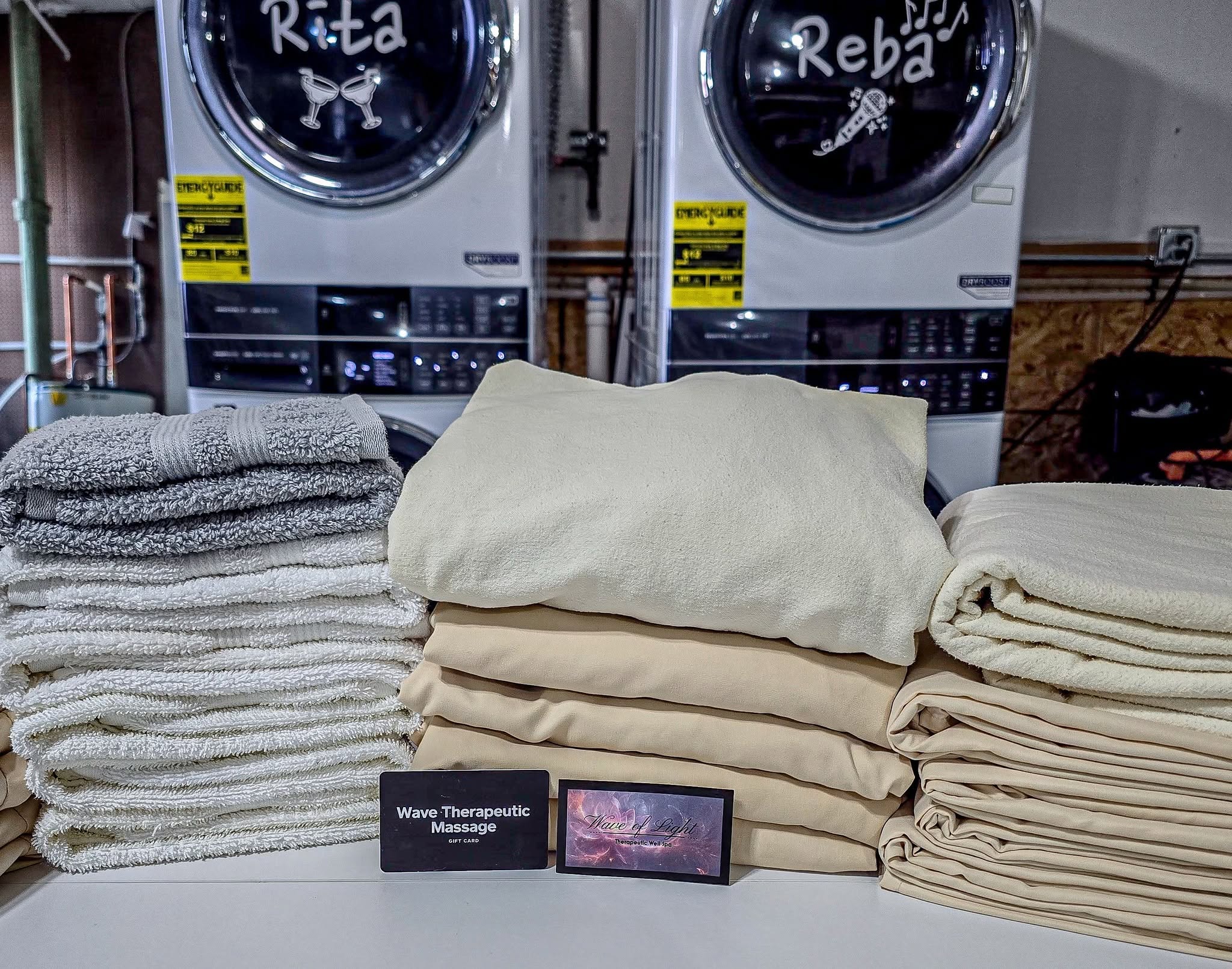 Freshly folded massage sheets and towels with Two Chicks commercial laundry machines in the background