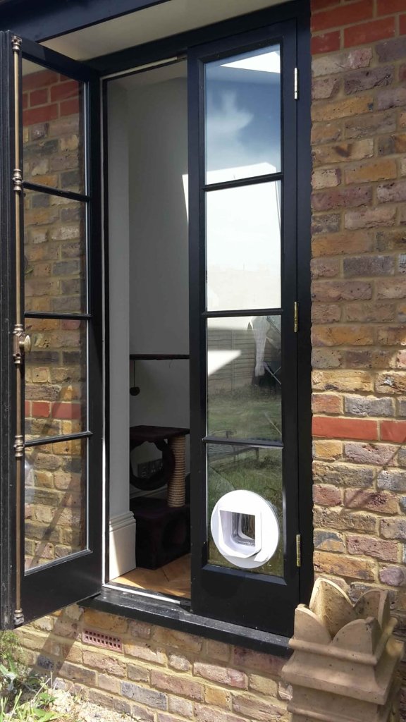 White cat flap installed in the lower pane of a black aluminium glazed door