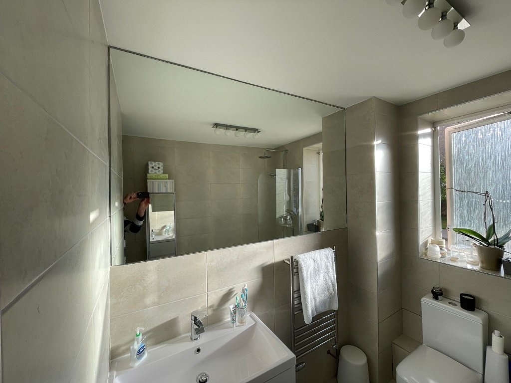 Large frameless bathroom mirror installed above a sink basin