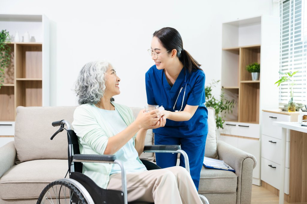 Caregiver offering water to an elderly woman in a living room