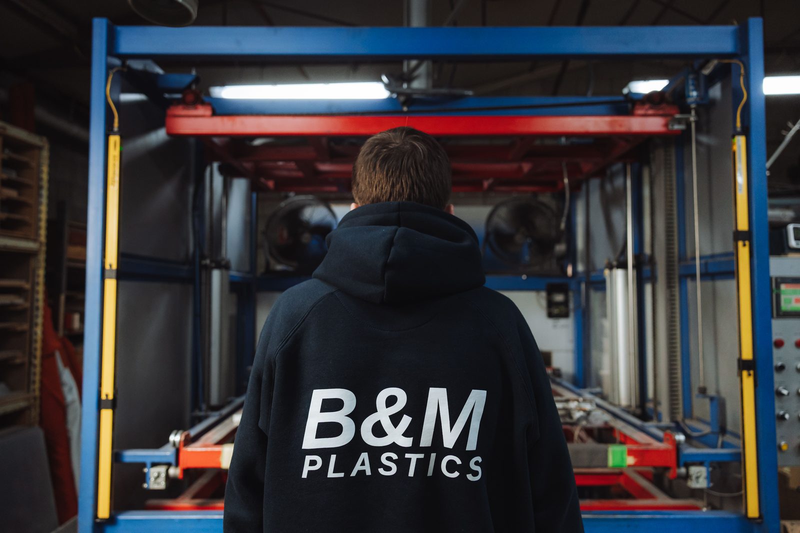 B&M Plastics technician in a branded hoodie standing in front of workshop machinery on the Yennora floor