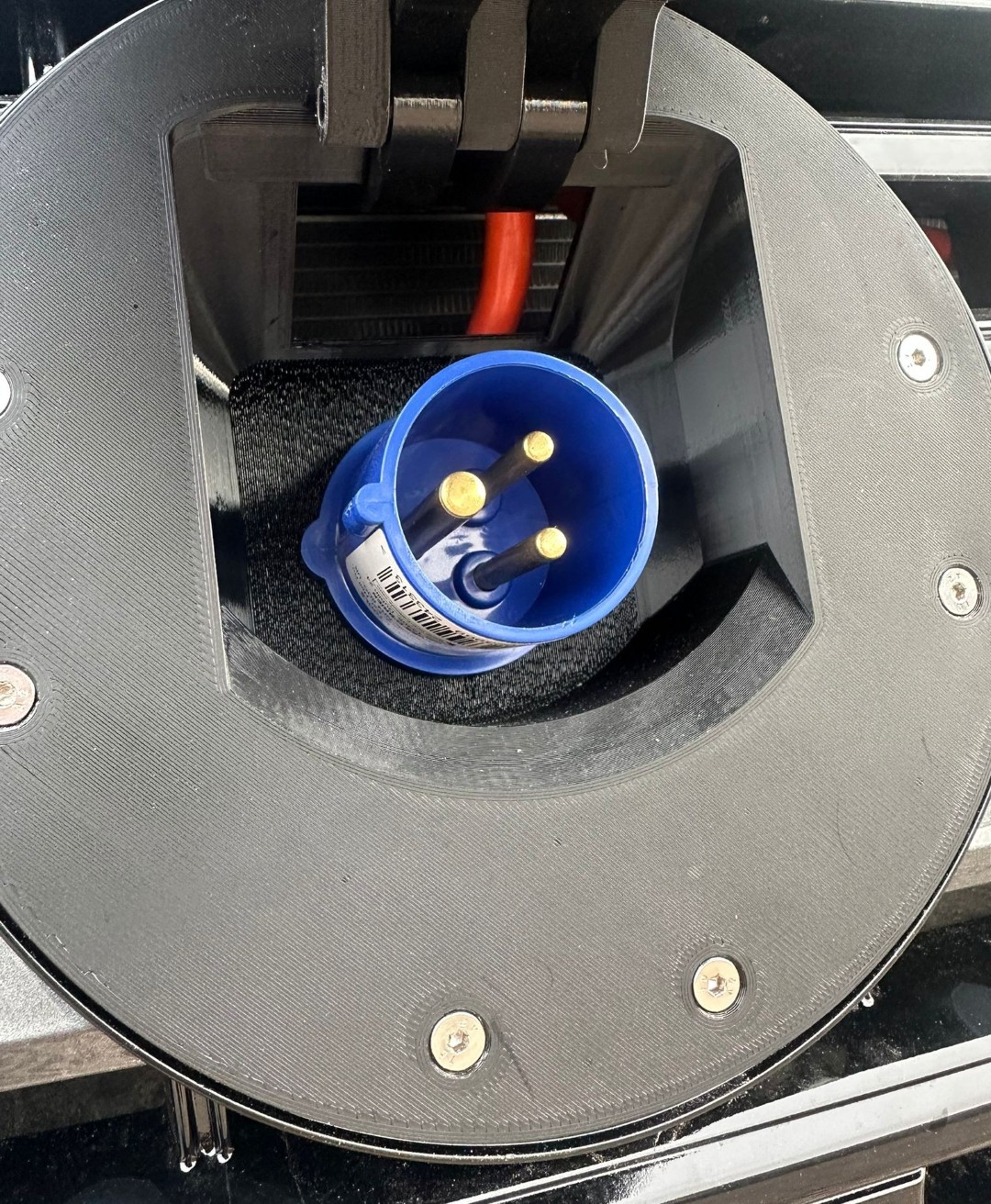 Charging port mount behind emblem