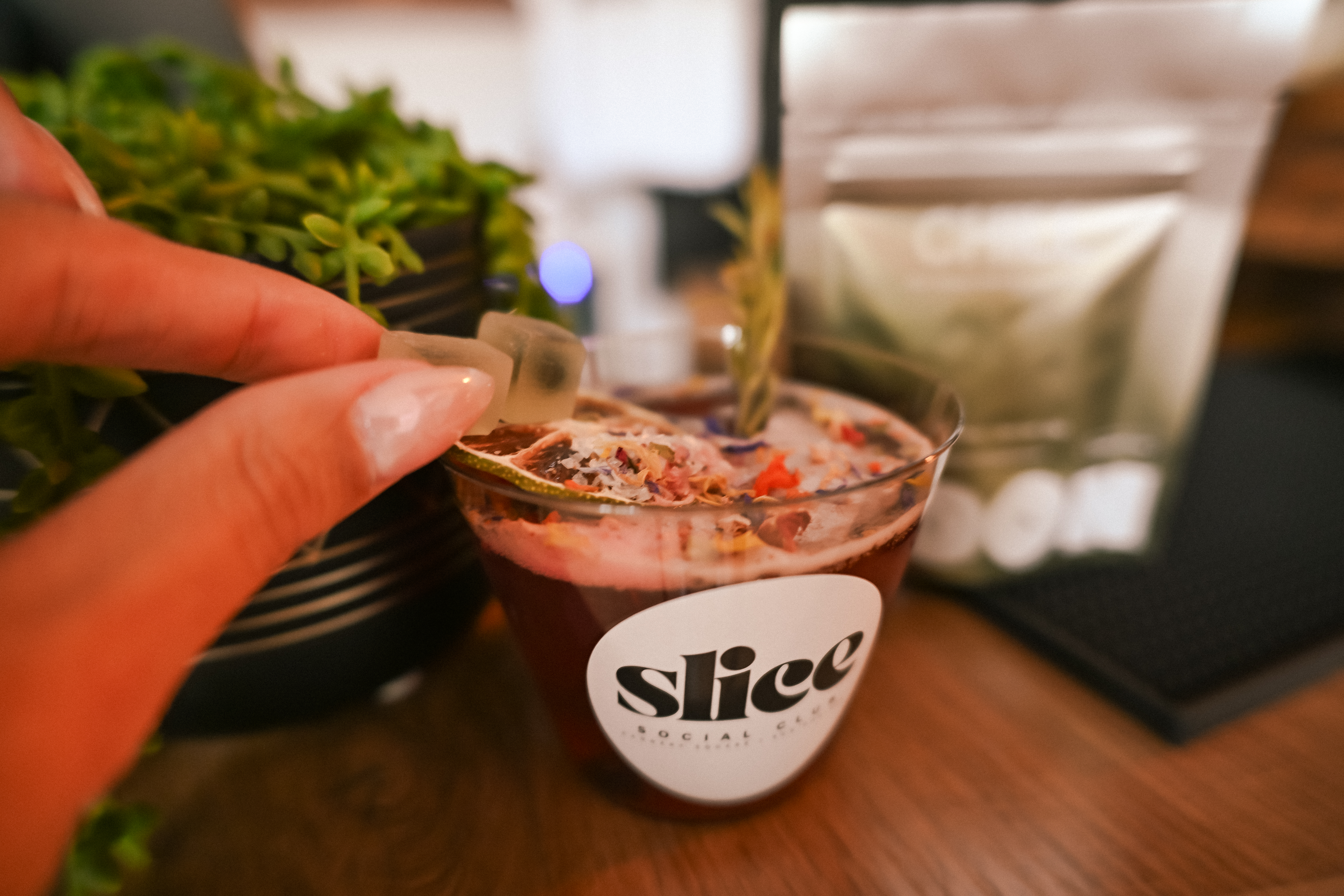 A hand holding a gummy beside a Slice Social Club mocktail