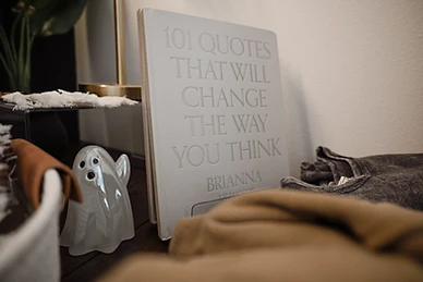 A book of quotes standing beside a ghost figurine on dark wood
