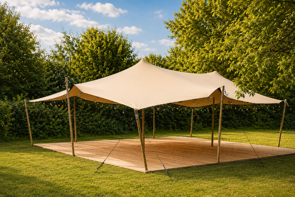 Tente stretch beige équipée d'un plancher en bois et de guirlandes dans un terrain arboré