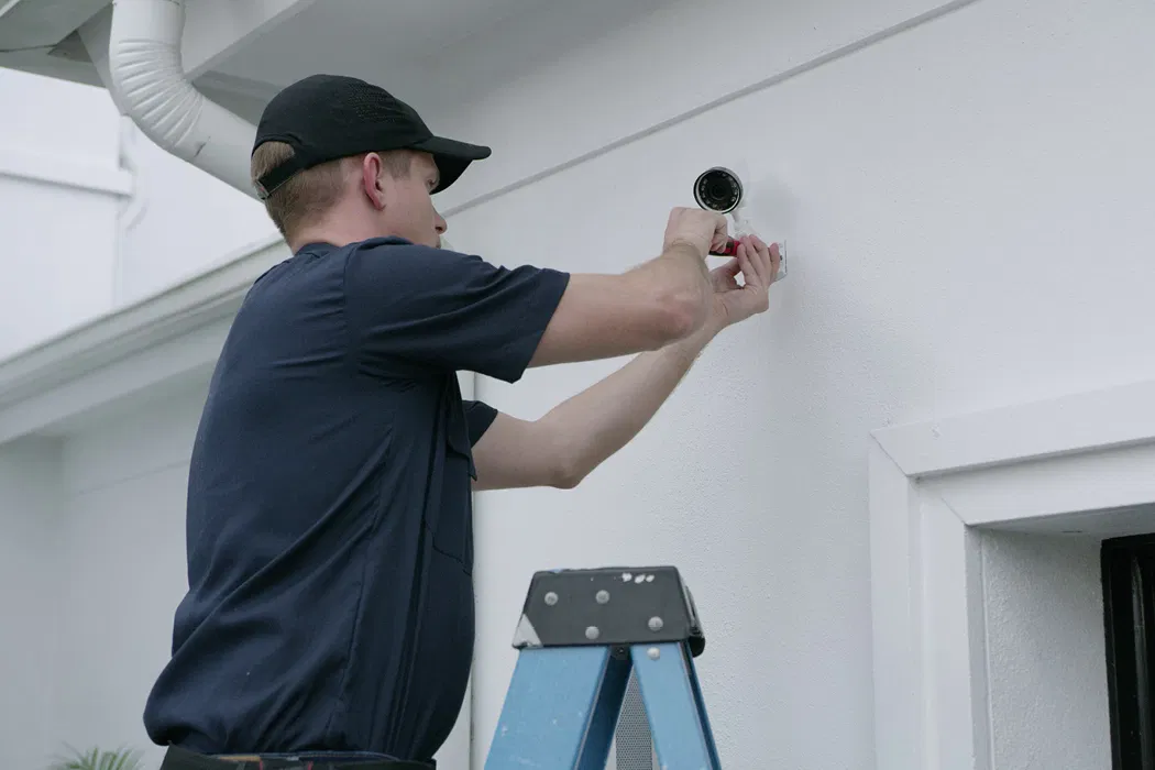 Technician installing a security camera under a roof eave