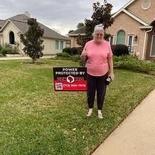 Senior woman giving thumbs up with Gen Pro Generators power protected sign at Houston area home