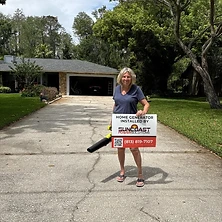 Woman holding Suncoast Power Solutions home generator sign in front of her Florida home
