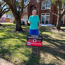 Homeowner giving thumbs up next to Gen Pro Generators power protected sign at Houston brick estate