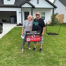 Two homeowners holding A&A GenPro emergency radio and remote in front of Houston Texas home