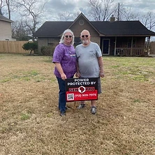 Couple holding Gen Pro Generators power protected sign in front of their Texas home