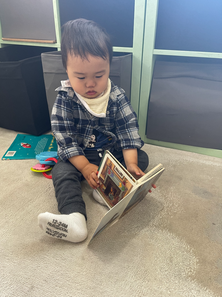 A toddler reading a book in front of the cubby shelves