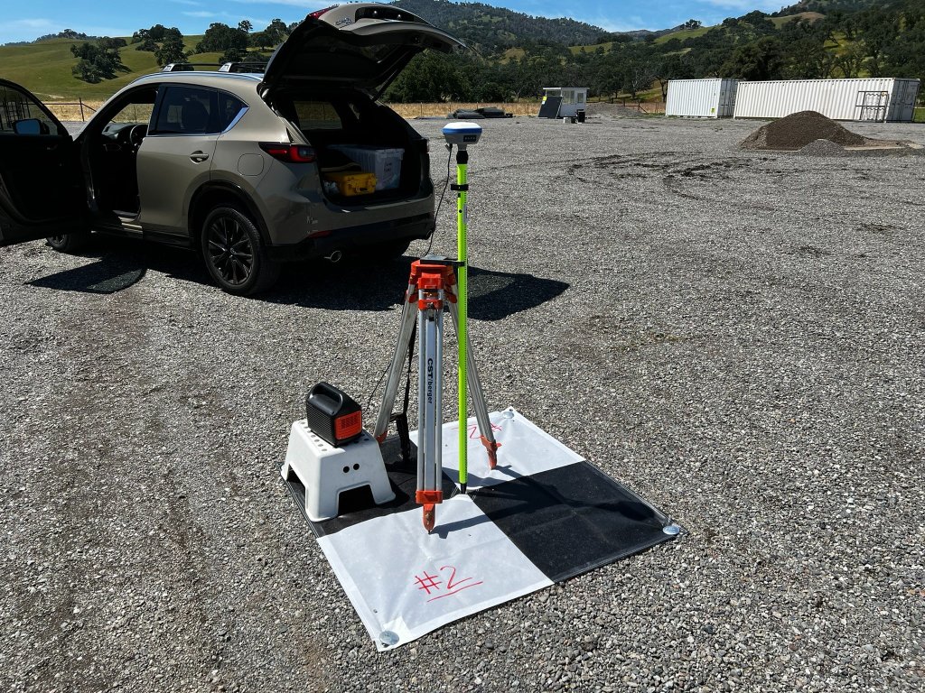 GNSS survey equipment and field-control setup beside a vehicle at an active project site.