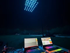 Ground-control computers beneath a coordinated aerial light display.