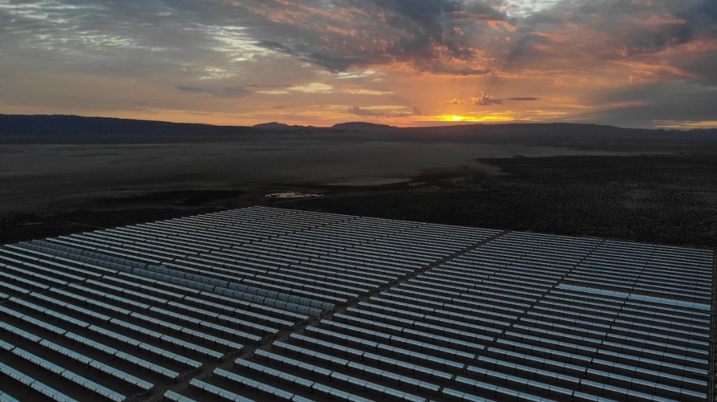 Utility-scale concentrated solar power field at sunset in a remote desert landscape.