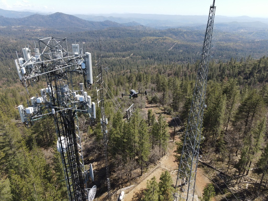 Drone operating near remote communications towers in a mountainous field environment.