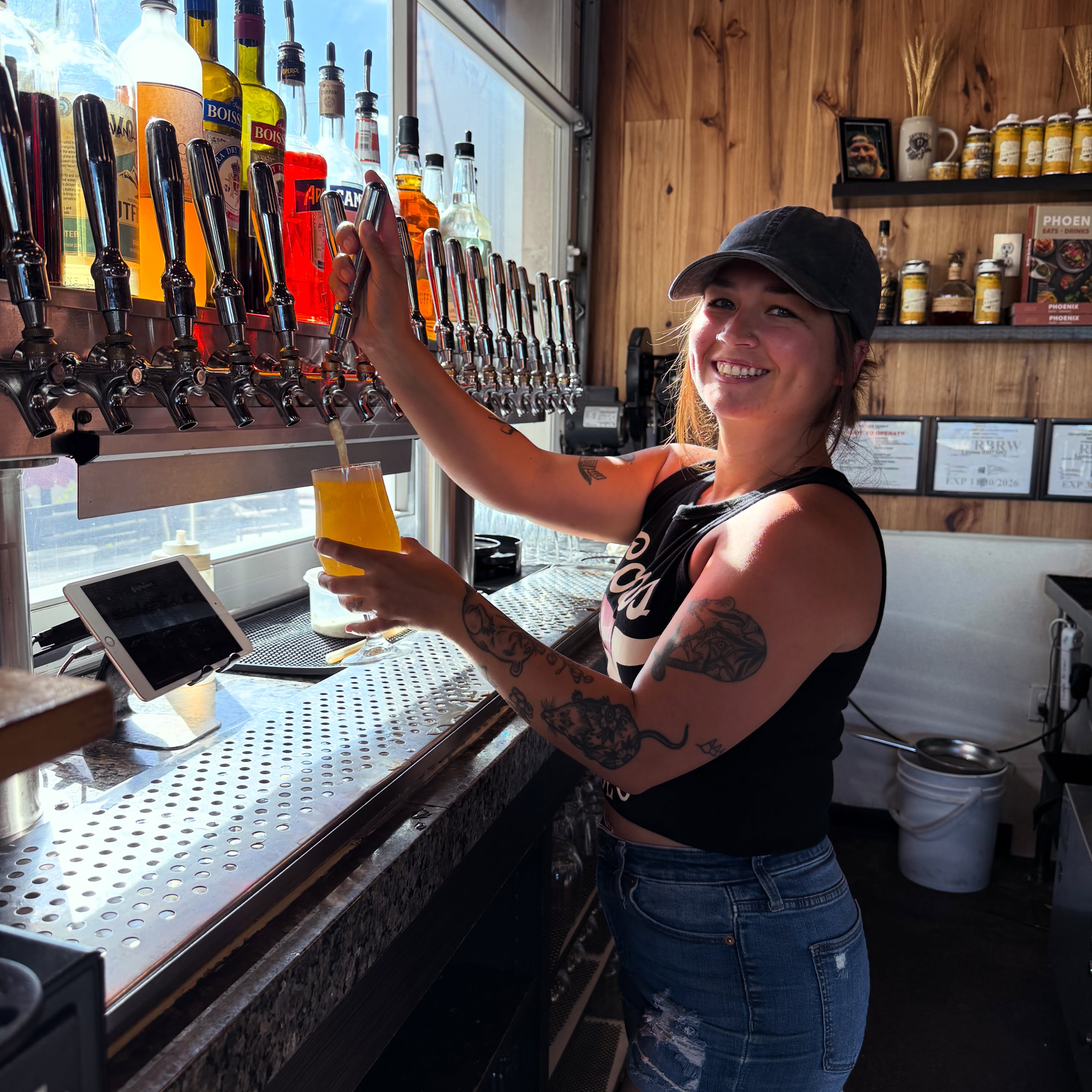 A bartender pouring a house beer at the tap wall inside Peoria Artisan Brewery
