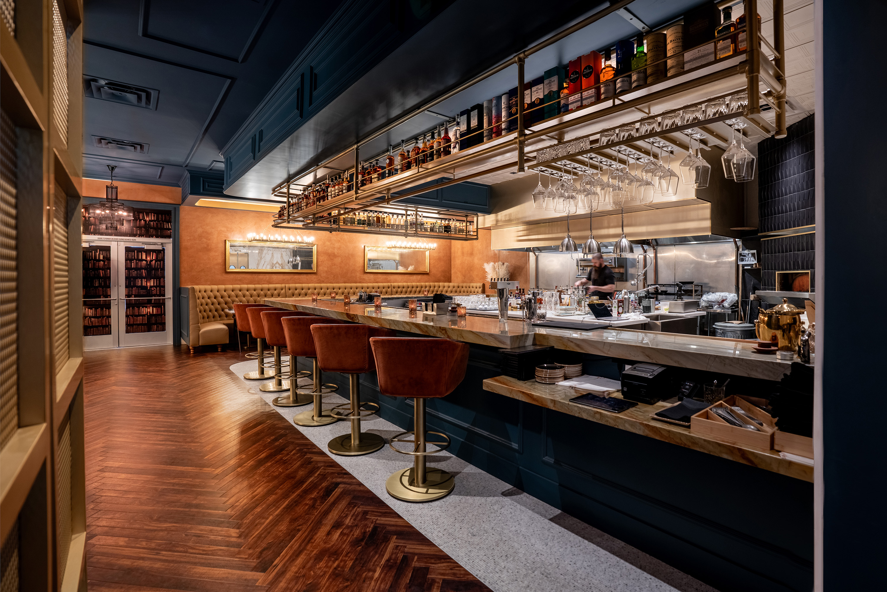 The marble bar inside Barley & Smoke, brass liquor racks above burnt-orange velvet stools