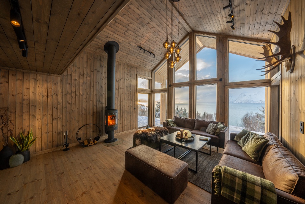 Open-plan living room with wood-burning stove and floor-to-ceiling fjord windows