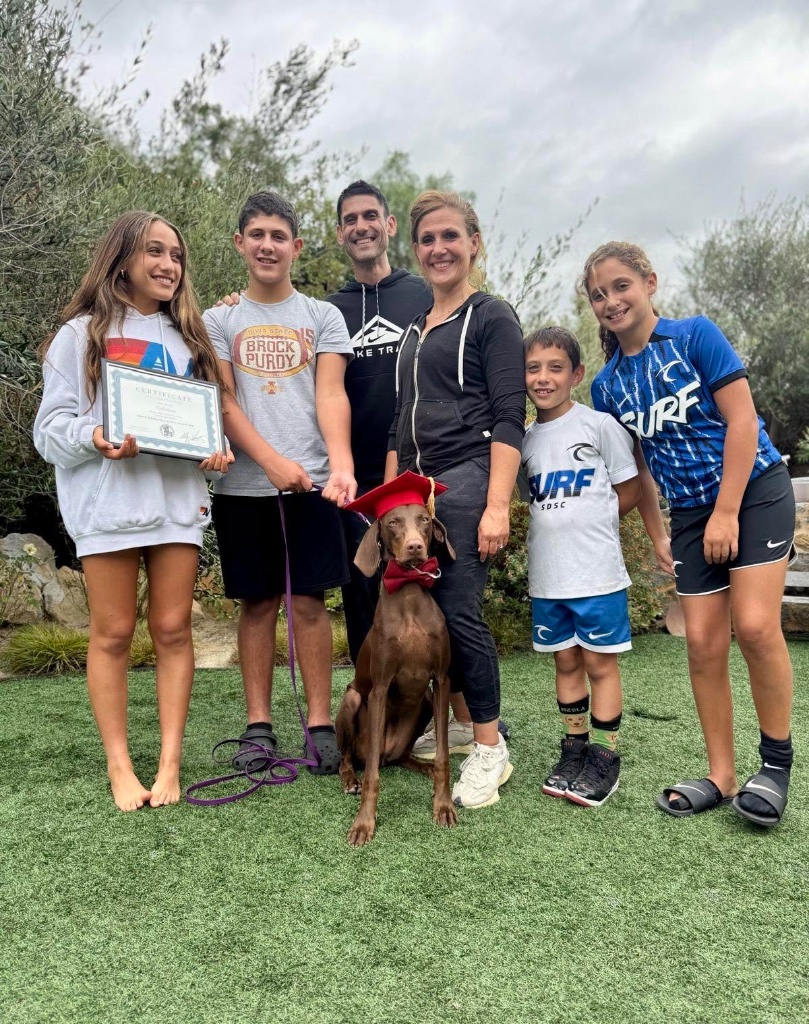 A family with their dog in a graduation cap and red bow tie.