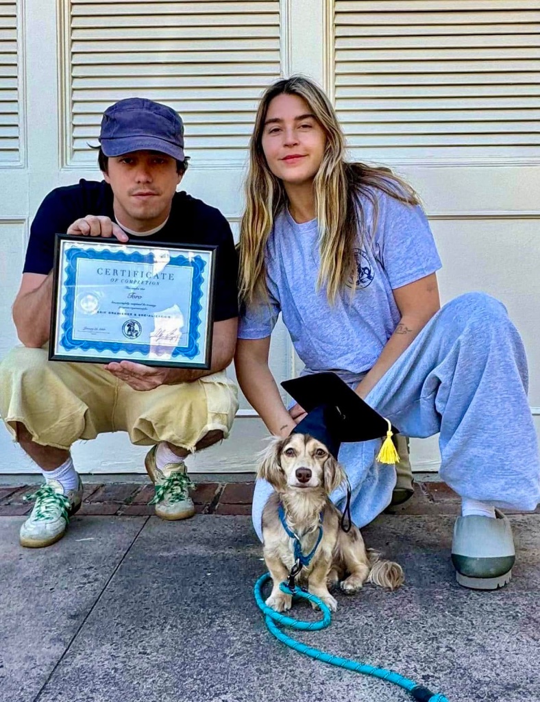 A couple crouching with their dog in a graduation cap, holding a certificate.