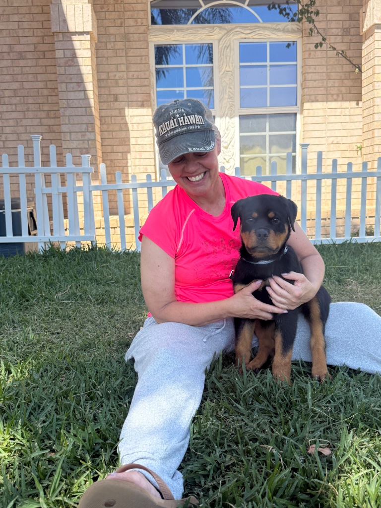 Johanna sits on the grass, cradling a Rottweiler puppy in her lap.