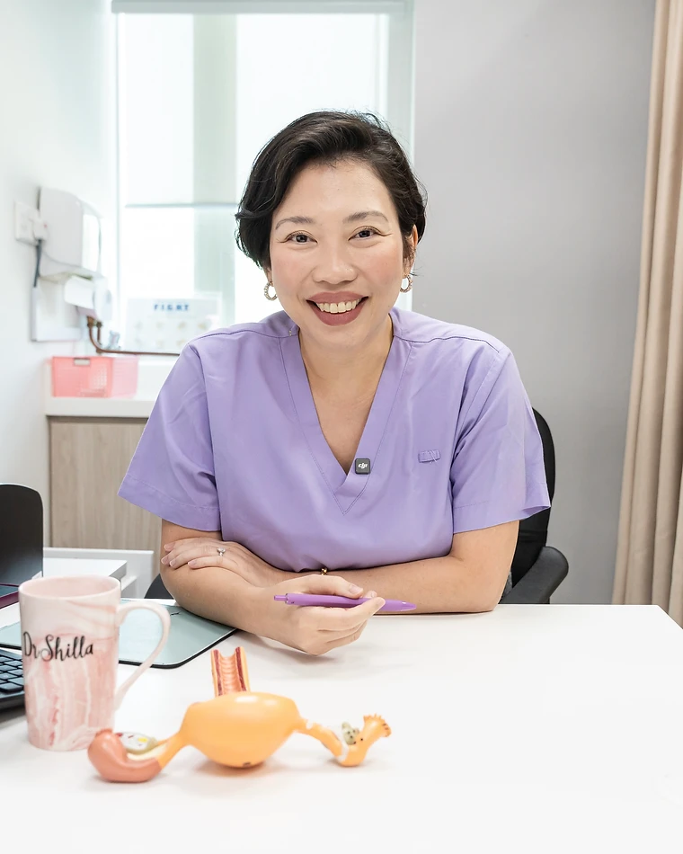 Dr Shilla Mariah Yussof seated at her consultation desk with a warm smile