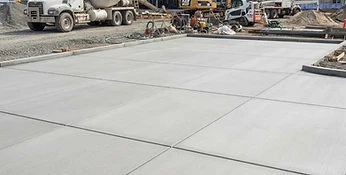 Large-scale finished commercial concrete pad with saw-cut joints and equipment in background