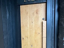 Exterior entry door — natural wood slab with custom pull handle and address numbers.