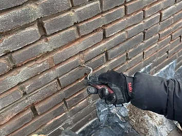 Dakdekker werkt de voegen van een bakstenen muur bij tijdens een daklekkage-reparatie