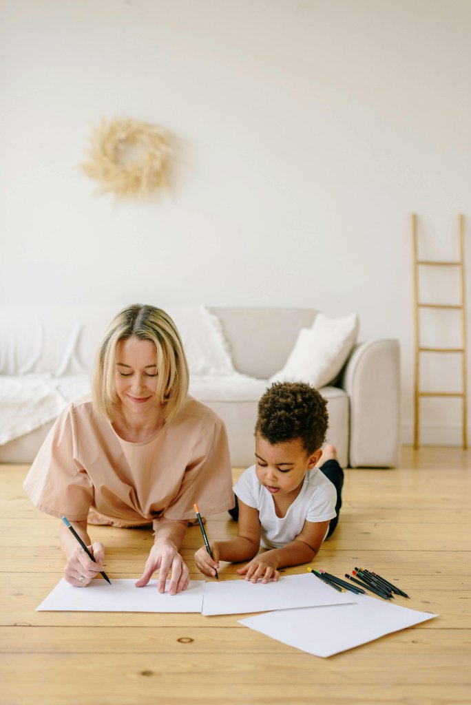 A nanny drawing alongside a child on the floor