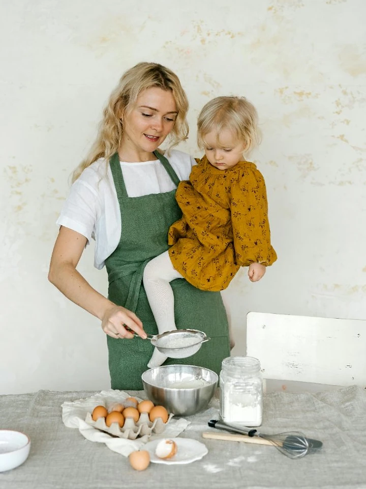 A nanny sifting flour with a child in a bright kitchen