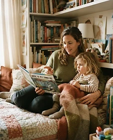 A nanny reading a picture book to a child in a reading nook