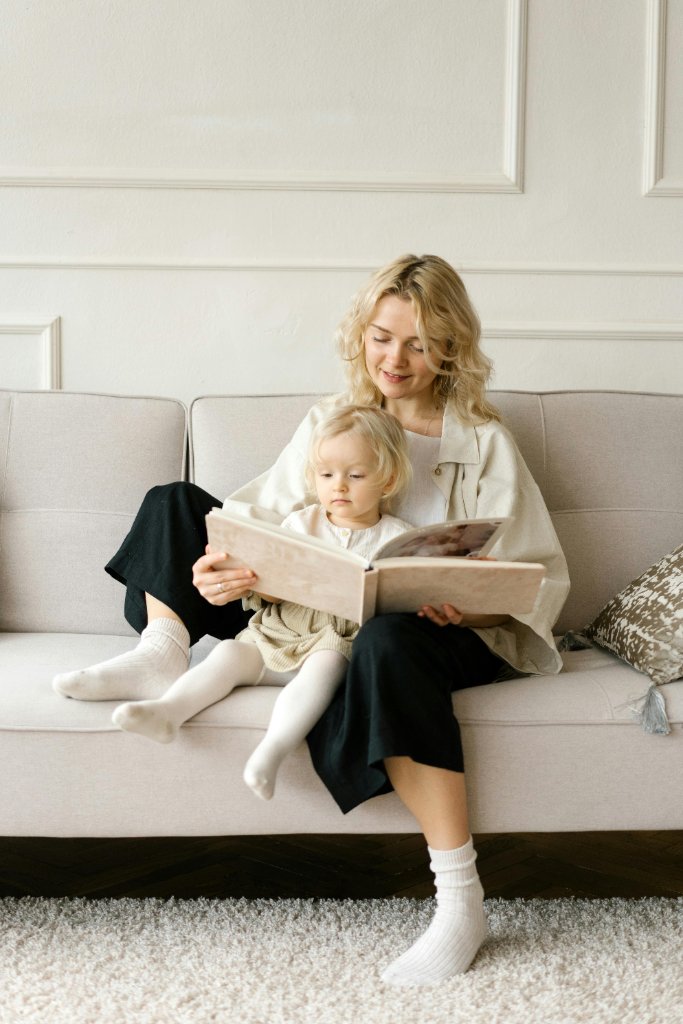 A nanny reading with a child on a soft couch