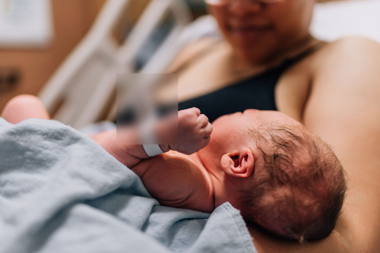 Close-up of newborn baby with hospital ID band, resting on mother