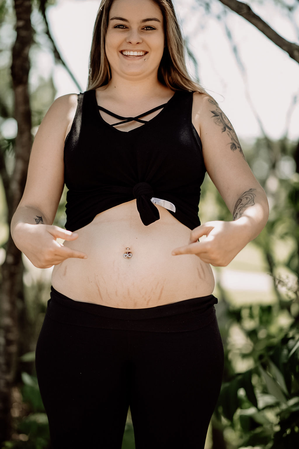 Pregnant woman smiling outdoors, pointing to her belly