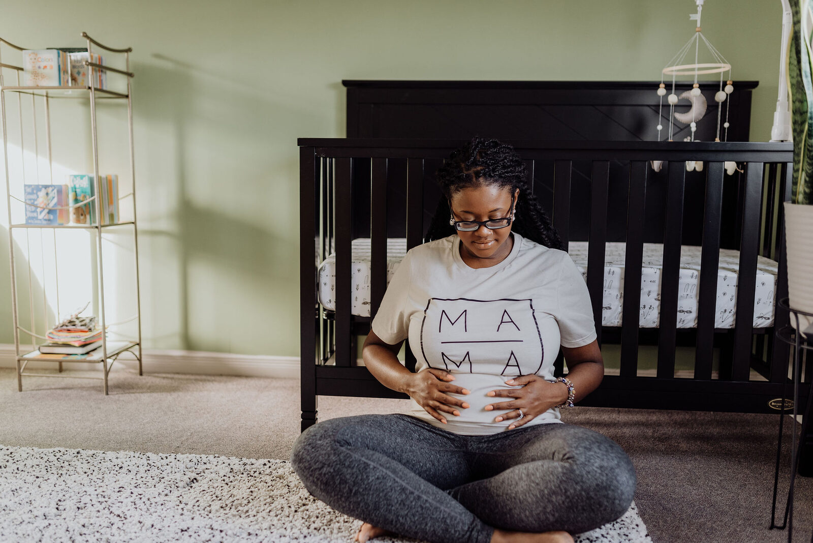 Pregnant woman in "Mama" shirt sitting in nursery preparing for baby