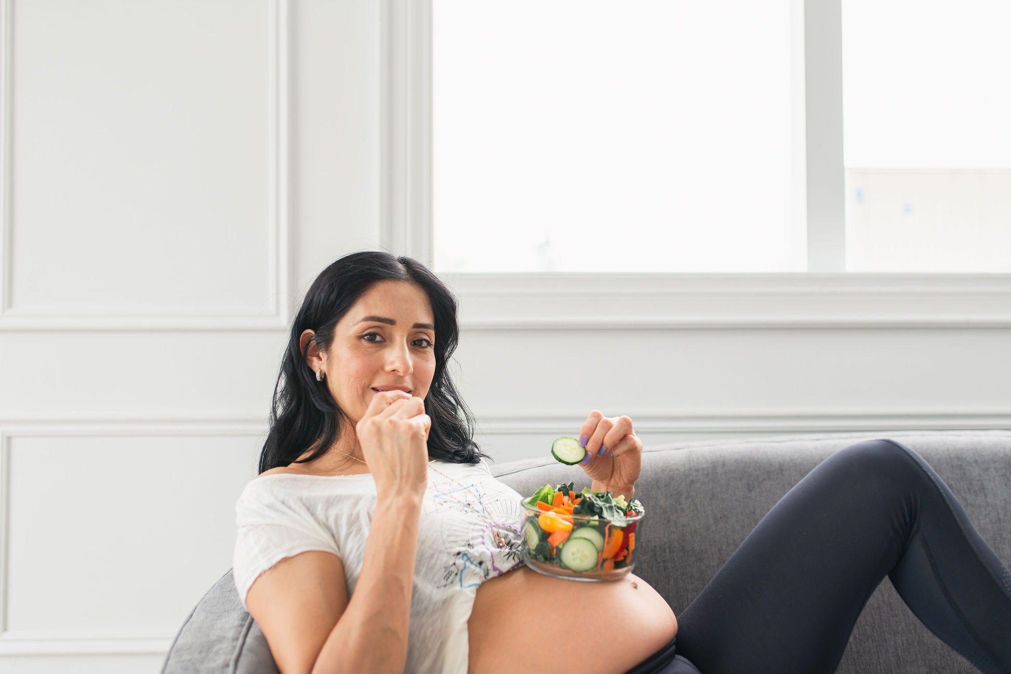 Pregnant woman eating a salad while resting on the sofa at home