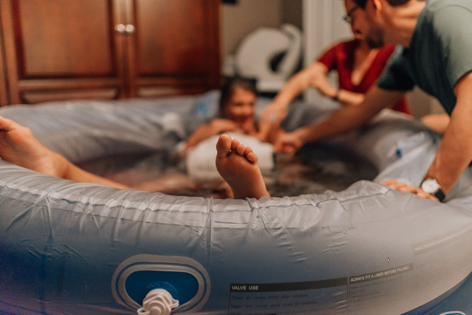 Woman in labor in a home birth pool supported by midwife and partner