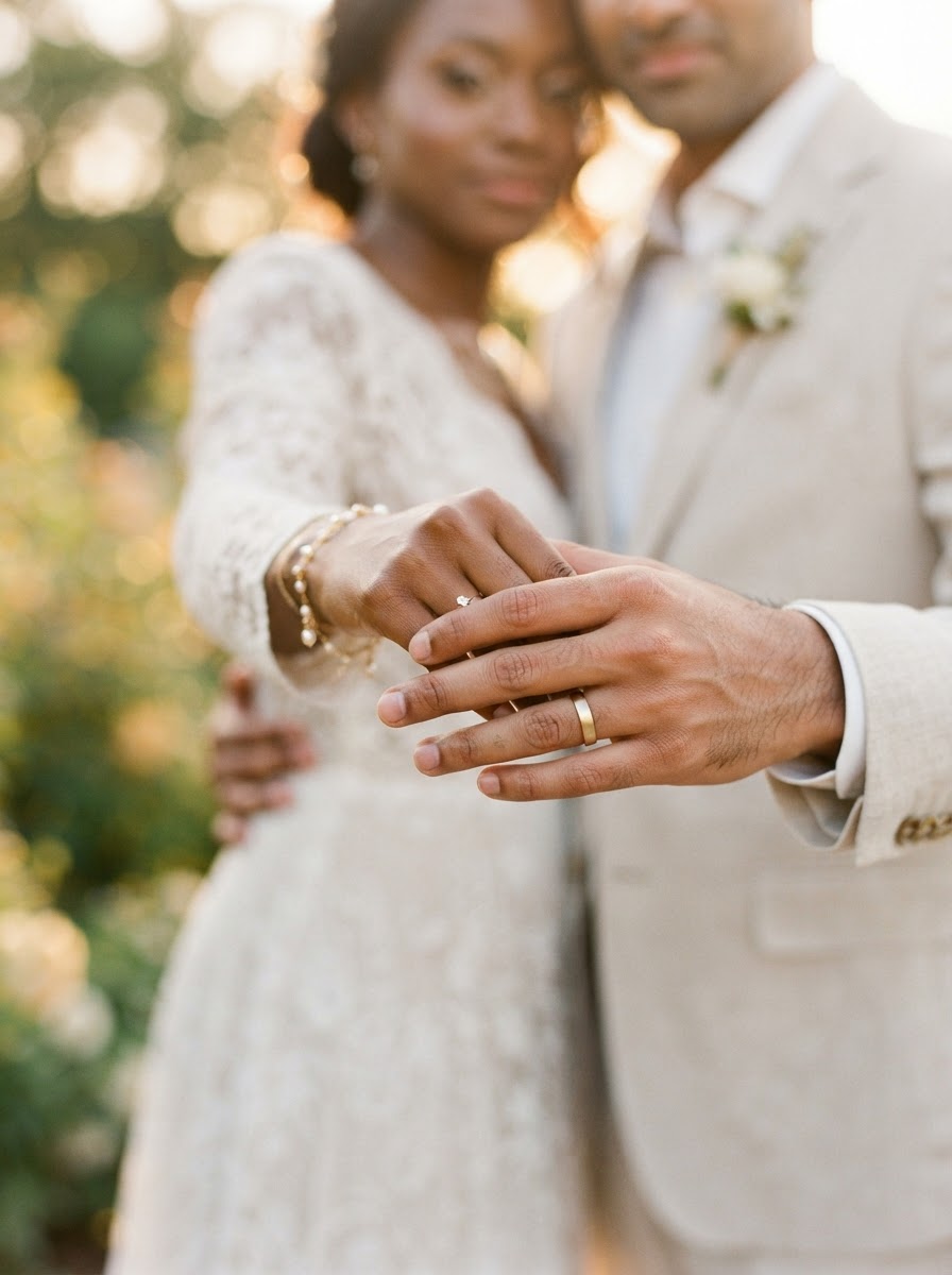 Couple holding hands with wedding bands in warm ivory light