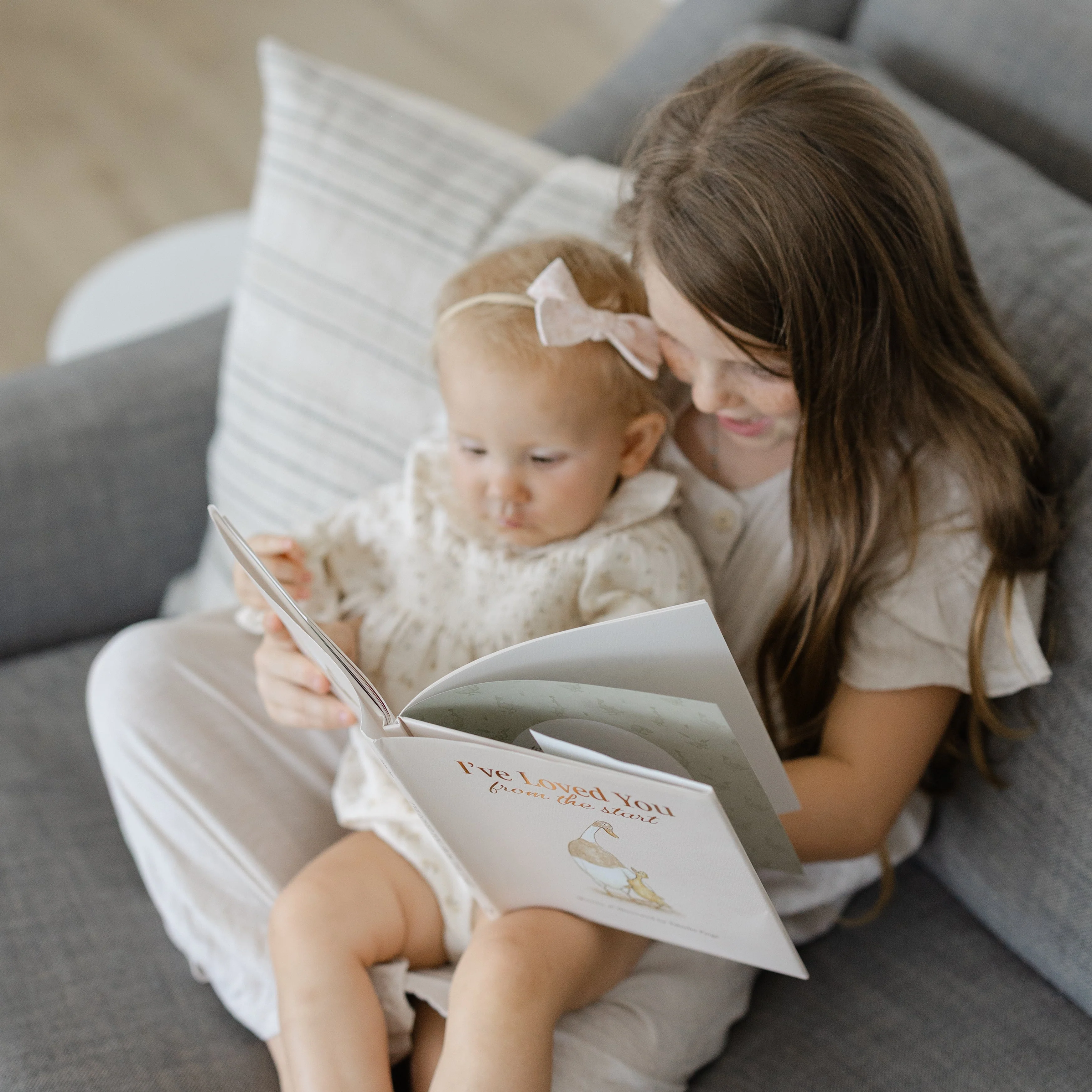 An older sibling reading the book to a baby on her lap