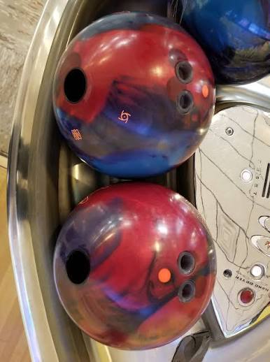 Two bowling balls showing pin up versus pin down drilling positions in a ball return unit