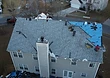 Installation underway — workers laying architectural shingles with safety harnesses in place.