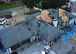 Bird's-eye view of the in-progress tear-off, with workers removing shingles and a debris dumpster staged on the driveway.