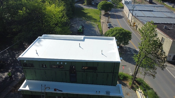 TPO membrane installation in progress, with ZIP System sheathing exposed and equipment staged on the lower roof.