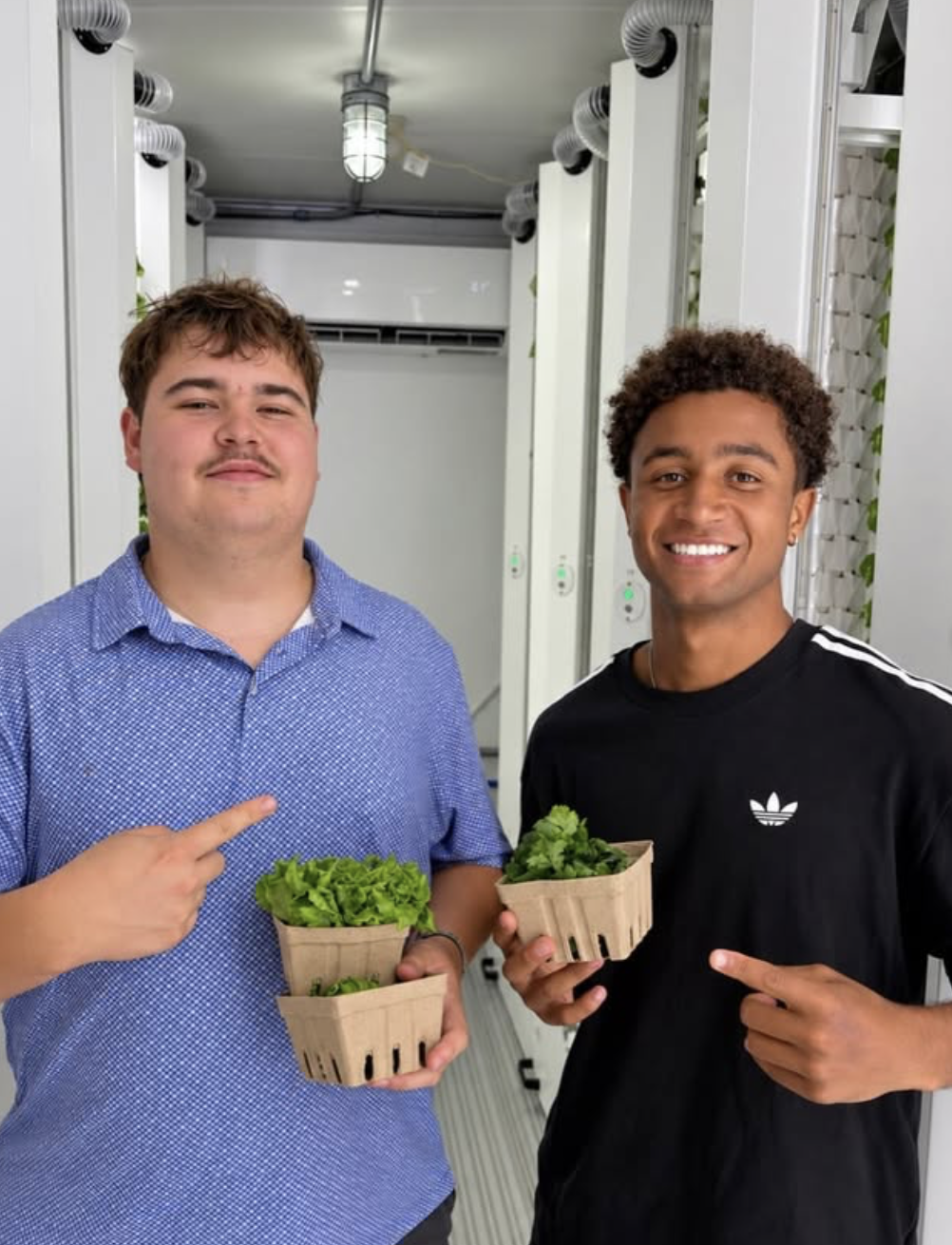 Two students showing baskets of freshly harvested greens