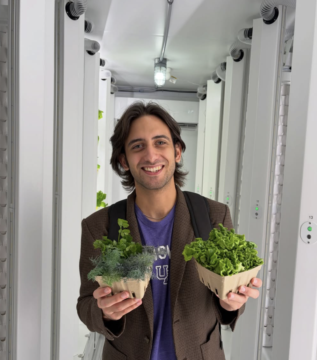Student holding baskets of fresh herbs and lettuce inside the container farm
