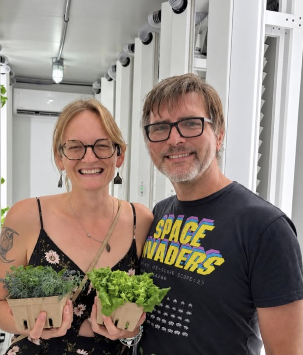 Two visitors holding baskets of fresh herbs and greens inside the farm
